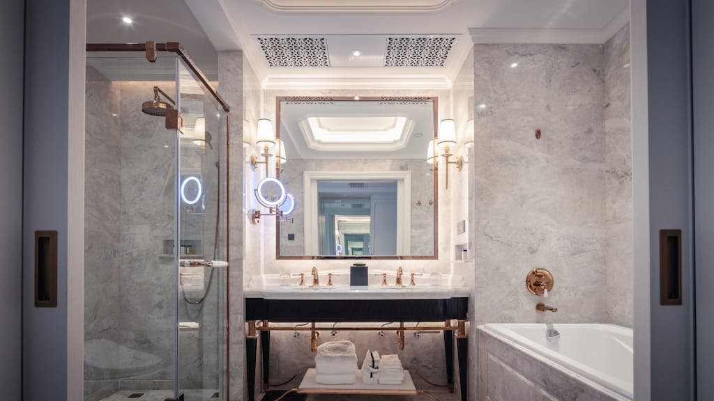 Photo by Hongyue Stone-Jon Lee Elegant bathroom featuring a marble sink, bathtub, and mirror with ambient lighting.